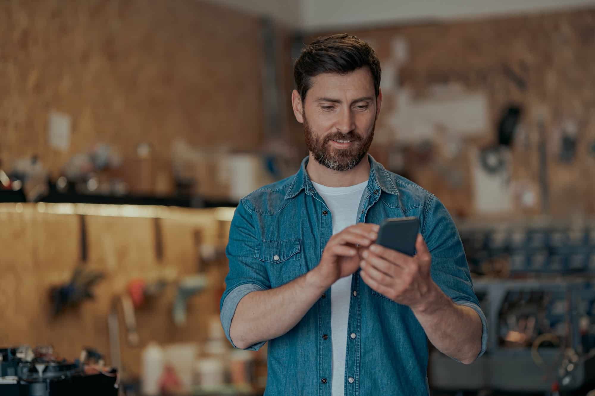 Male property maintenance worker in storage room using mobile app on his phone