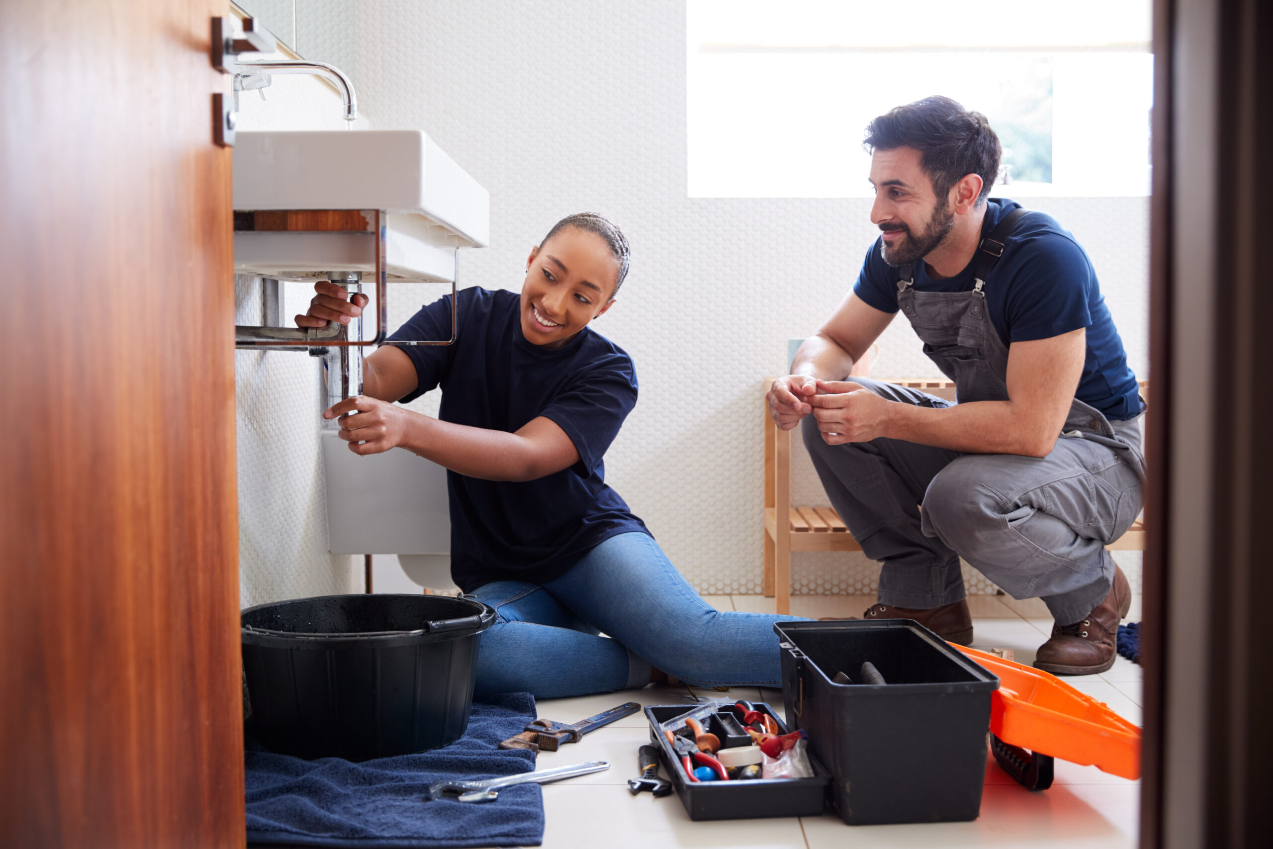 Plumber teaching an apprentice to fix leaking sink in an apartment building